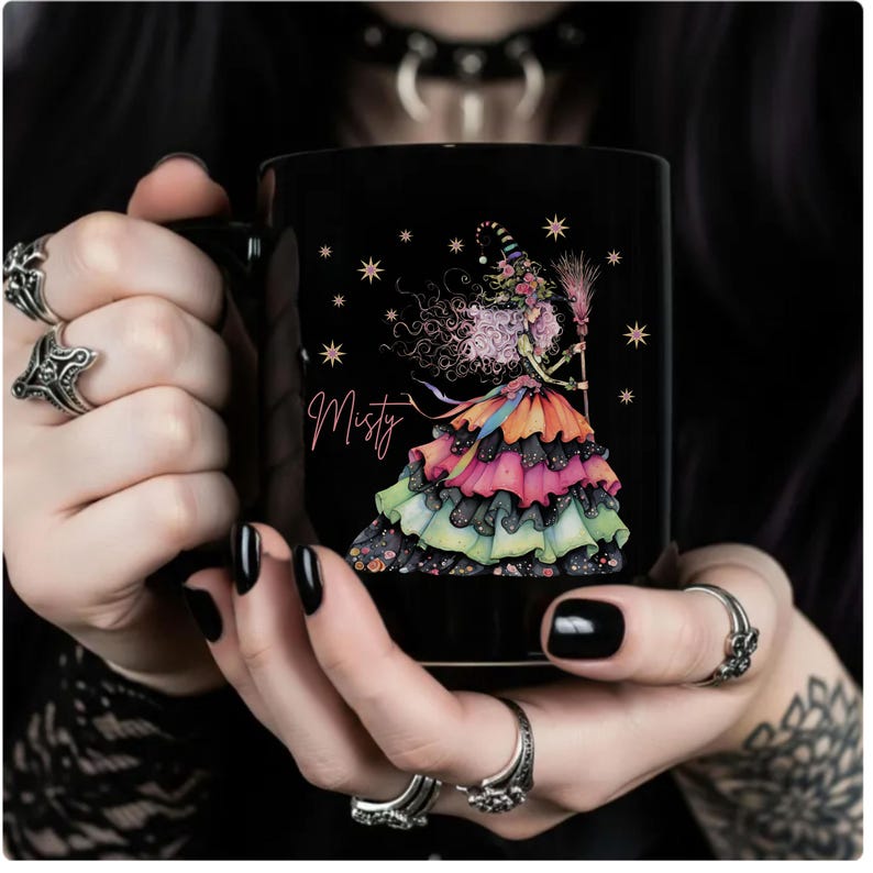 Puede incluir: Taza de cer&aacute;mica negra con una colorida ilustraci&oacute;n de una bruja con una escoba y el nombre "Misty". La bruja lleva un vestido en capas con volantes rosas, naranjas, negros y verdes. El dise&ntilde;o incluye estrellas y un estilo caprichoso.