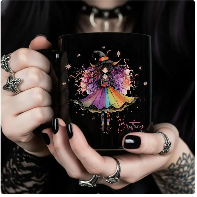 Puede incluir: Taza de cer&aacute;mica negra con una ilustraci&oacute;n de una bruja con pelo colorido y un vestido arco&iacute;ris. La taza tiene el nombre "Brittany" en escritura cursiva. El dise&ntilde;o incluye estrellas y un sombrero de bruja.
