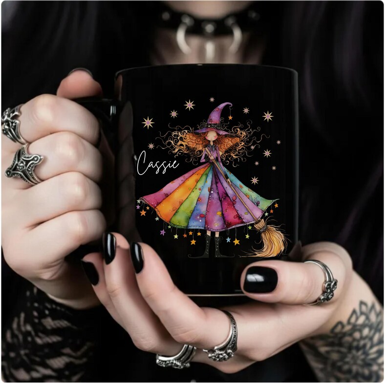 Puede incluir: Taza de cer&aacute;mica negra con una ilustraci&oacute;n de una bruja con un vestido arco&iacute;ris, sosteniendo una escoba. La taza tiene el nombre "Cassie" en escritura cursiva y est&aacute; decorada con estrellas. Un regalo &uacute;nico para los fan&aacute;ticos de la fantas&iacute;a y la magia.