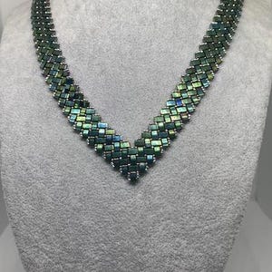 Peut inclure: Un collier de perles vert et argent irisé avec un design en V.
