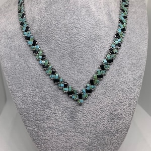 Op de afbeelding: Een zwarte en turquoise kralenketting met een chevron-patroon.