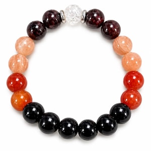May include: A beaded bracelet featuring a circular arrangement of polished gemstone spheres in shades of black, orange, red, and dark brown, accented by a single clear crackle glass bead at the top flanked by two small silver-toned metal spacers.