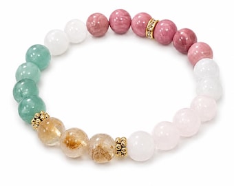 Puede incluir: Una pulsera elástica de cuentas que presenta una variedad de piedras redondas en tonos verde, blanco, rosa y amarillo dorado. El diseño incluye pequeños espaciadores de metal dorado y una cuenta decorativa dorada con cristales transparentes.