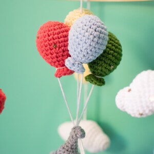 May include: A baby mobile with crocheted clouds, a dinosaur, and balloons in shades of red, green, blue, and yellow.