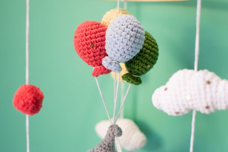 May include: A baby mobile with crocheted clouds, a dinosaur, and balloons in shades of red, green, blue, and yellow.