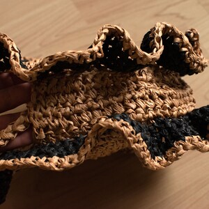 May include: A brown straw hat with a black crocheted trim. The hat has a wide brim and a ruffled edge.