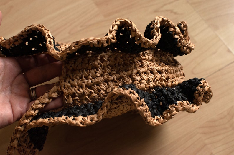 May include: A brown straw hat with a black crocheted trim. The hat has a wide brim and a ruffled edge.