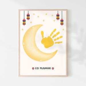 May include: A framed art print featuring a yellow crescent moon and a handprint. The print includes hanging lanterns, stars, and the text "EID MUBARAK" in red. The artwork is set against a white background.