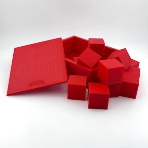 Könnte beinhalten: Ein rotes geometrisches Puzzleset. Das Set enthält eine Box mit Deckel und mehrere rote Würfelblöcke. Die Box ist geöffnet und der Deckel ist teilweise geöffnet. Die Blöcke sind um die Box herum verstreut.