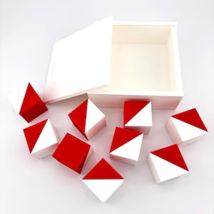 May include: A white wooden box with a partially open lid, surrounded by ten small, square blocks. Each block is divided diagonally, with one half painted red and the other white. The blocks are scattered around the box.