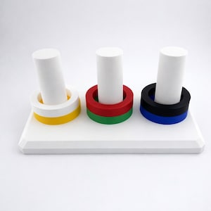 May include: A white wooden toy with three vertical white cylinders. Each cylinder is surrounded by colorful rings: yellow and white, red and green, and black and blue. The toy sits on a white rectangular base.