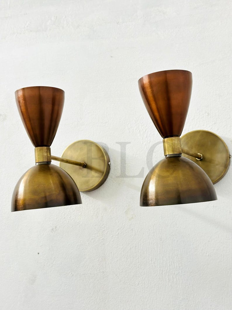 May include: Two vintage-style wall sconces. Each sconce features a copper-colored, cone-shaped shade atop a brass-colored, rounded base. The sconces are mounted on circular brass backplates, creating a warm, inviting aesthetic.