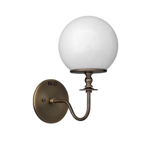 May include: A wall-mounted sconce featuring a white globe shade and a bronze-colored metal base. The fixture has a curved arm and a round backplate. The letters "BLC" are visible on the backplate.