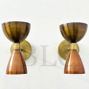 May include: Two vintage-style wall sconces. Each sconce features a copper-colored, cone-shaped shade and a brass-colored, bowl-shaped top. The sconces are mounted on round brass backplates, creating a warm, inviting aesthetic.