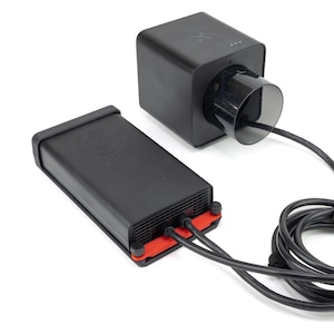 May include: A black power adapter with a red accent and a black power cord connected to a black cube-shaped device with a black circular opening.