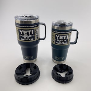 Op de afbeelding: Twee YETI Rambler reistassen, een in donkerblauw en een in tealgroen, met zwarte deksels en zwarte rubberen bodems. De bekers zijn respectievelijk 30 oz en 20 oz. De tekst op de bekers luidt "YETI Rambler 30 oz Travel Mug" en "YETI Rambler 20 oz Travel Mug".