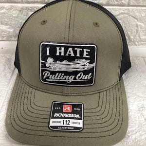May include: Olive green trucker hat with a black mesh back. The front patch reads "I HATE Pulling Out" with a boat graphic. Features a Richardson 112 Trucker tag. Adjustable fit.