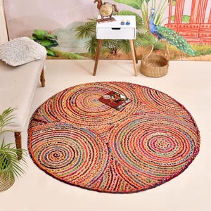 Può includere: Un grande tappeto rotondo con un motivo a spirale nei toni del rosso, arancione, giallo e blu. Il tappeto è realizzato in materiale tessuto e ha una superficie strutturata. Una rivista è posizionata sul tappeto.