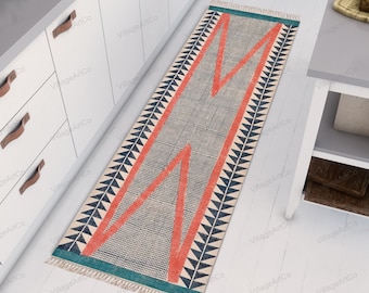 Puede incluir: Una alfombra larga y estrecha con un patrón geométrico en tonos rojos, azules y blancos. La alfombra tiene un borde con flecos y está hecha de un material tejido.