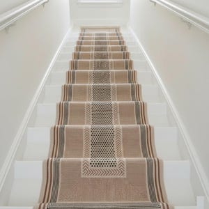 Puede incluir: Una alfombra de escalera con estampado beige y marrón instalada en escaleras blancas. La alfombra presenta diseños geométricos, incluyendo rayas, chevrones y patrones de puntos. La escalera tiene paredes blancas y una ventana en la parte superior.