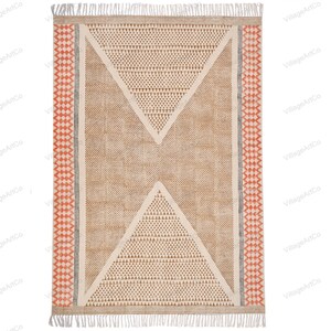 May include: A beige and brown geometric patterned rug with a white fringe border. The rug has a red and black diamond pattern along the edges.