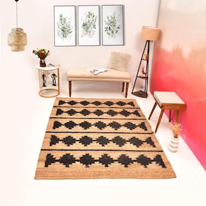 May include: A rectangular jute rug with a geometric black diamond pattern. The rug is placed in a room with a bench, artwork, and a floor lamp. The room has a neutral color palette with pops of red.