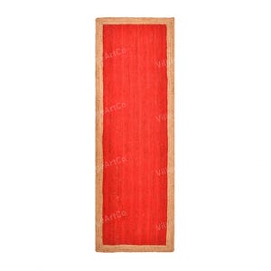 Puede incluir: Una alfombra rectangular de yute rojo con un borde de fibra natural. La alfombra tiene una textura tejida y es adecuada para uso en interiores. Las dimensiones de la alfombra son de aproximadamente 60 cm de ancho y 152 cm de largo.