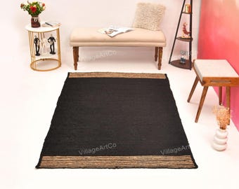 May include: A rectangular black jute rug with a natural tan border. The rug is displayed on a white surface. The words "VillageArtCo" are printed on the rug. This rug is suitable for living rooms and bedrooms.