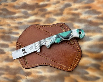 May include: A small, green and white marbled pocket knife with a decorative handle and a serrated blade. The blade has a ruler and a small design of a couple getting engaged.