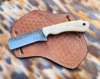Puede incluir: Un cuchillo pequeño, azul y blanco, dentado, con mango de hueso. El cuchillo está en una funda de cuero marrón con un patrón tejido.