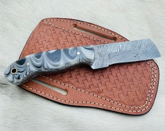 May include: A knife with a black and white patterned handle and a Damascus steel blade. The knife is in a brown leather sheath.