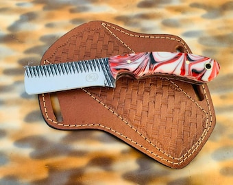 Puede incluir: Un pequeño cuchillo decorativo con un mango veteado rojo, blanco y negro descansa sobre una funda de cuero marrón. La hoja del cuchillo tiene un borde dentado. La funda tiene un patrón tejido y está cosida con hilo blanco.