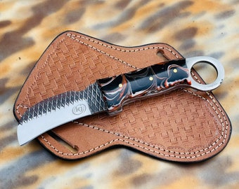 May include: A curved, stainless steel knife with a black and red marbled handle. The knife has a serrated edge and a small hole in the handle. The knife is in a brown leather sheath with a woven pattern.
