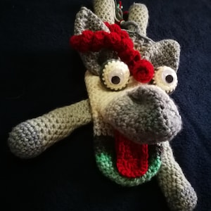 May include: A crocheted gray, white, and green plush toy with red details. The toy has large white eyes, a red tongue, and a red crocheted horn.