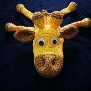 May include: A crocheted giraffe toy with brown and yellow yarn. The giraffe has large, white eyes and a brown nose.