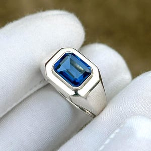 May include: A silver ring with a rectangular, vibrant blue gemstone. The gemstone is set in a polished silver band. The ring is shown against a white background.