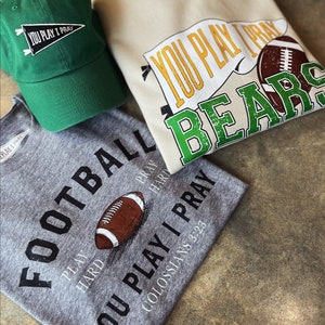 May include: Three shirts with a football theme. One gray shirt says "Football Play Hard Pray Hard You Play I Pray Colossians 3:23". One white shirt says "You Play I Pray Bears" with a green and yellow pennant and a brown football. One green shirt says "You Play I Pray" with a black pennant.