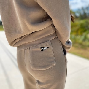 May include: A pair of brown sweatpants with a back pocket featuring a black embroidered patch that says "YIPIP".