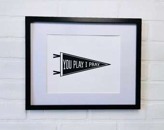 May include: Black and white print of a pennant with the text "YOU PLAY I PRAY" in a black frame.