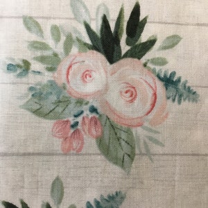 May include: Floral fabric with a watercolor design. The pattern features pink roses, green leaves, and blue-green accents. The background has a light wood grain pattern. The fabric is likely used for home decor or crafting projects.