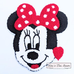May include: A red and white felt applique of Minnie Mouse with a red bow and a red heart. The applique is on a white background.