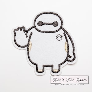 May include: White embroidered patch featuring a cartoon character with a black outline. The character has a rounded body, a small circle on the chest, and is waving. The patch has a white background and the text "Kiki's Tiki Room".