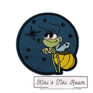 May include: A blue and yellow embroidered patch of a cartoon firefly with a big smile, against a dark blue background with white stars.