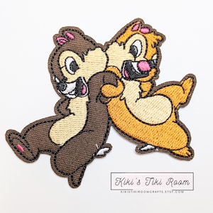 May include: Embroidered patch featuring Chip and Dale from Disney's Chip 'n Dale Rescue Rangers. The patch shows Chip and Dale hugging, with Chip on the left and Dale on the right. Chip is brown and Dale is orange.