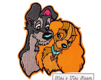 Puede incluir: Parche bordado con Lady y la Tramp, una pareja clásica de Disney. El parche muestra a Lady, un cocker spaniel marrón y blanco, con la cabeza apoyada en Tramp, un perro callejero negro y gris. El parche está sobre un fondo naranja.