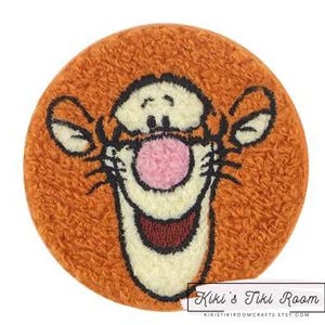 May include: Orange and brown plush embroidered patch featuring the face of Tigger from Winnie the Pooh. The patch has a pink nose and a white smile.