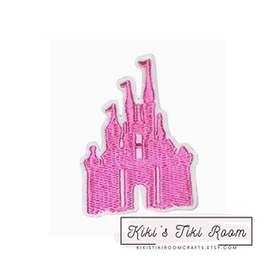 May include: Pink felt embroidered patch of a fairytale castle with a pointed roof and multiple towers. The castle is outlined in white and has a pink interior.