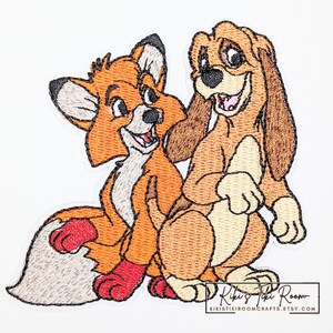May include: Embroidered patch featuring Tod the fox and Copper the hound dog from the Disney film, The Fox and the Hound. The patch is mainly orange, brown, and white, with black accents. The patch has the text "Kiki's Tiki Room" at the bottom.