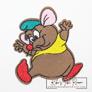 May include: Embroidered patch featuring a cartoon mouse in a running pose. The mouse is brown with a yellow vest, red shoes, and a green hat. The patch has a brown border and the text "Kiki's Tiki Room" at the bottom.