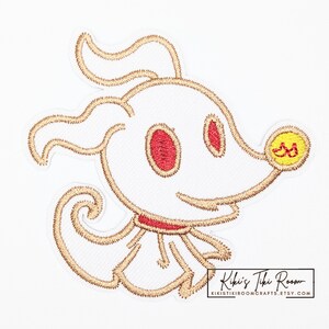 Peut inclure: Écusson brodé représentant un chien de dessin animé blanc avec des yeux rouges et un collier rouge. Le chien a un contour doré et un nez jaune. L'écusson est sur fond blanc. Le texte "Kiki's Tiki Room" est en bas à droite.